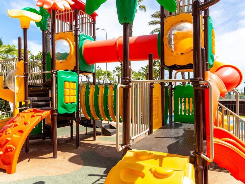 Bunter Kinderspielplatz mit Rutschen, Klettergerüsten und Tunnel aus Kunststoff und Metall.