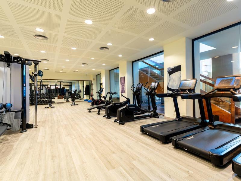 Großer Fitnessraum mit Holzfußboden, Laufbändern, Trainingsgeräten und Spiegelwand.