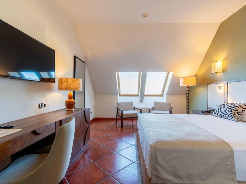 Helles Hotelzimmer mit Doppelbett, Holzschreibtisch, Sesseln und großen Dachfenstern.