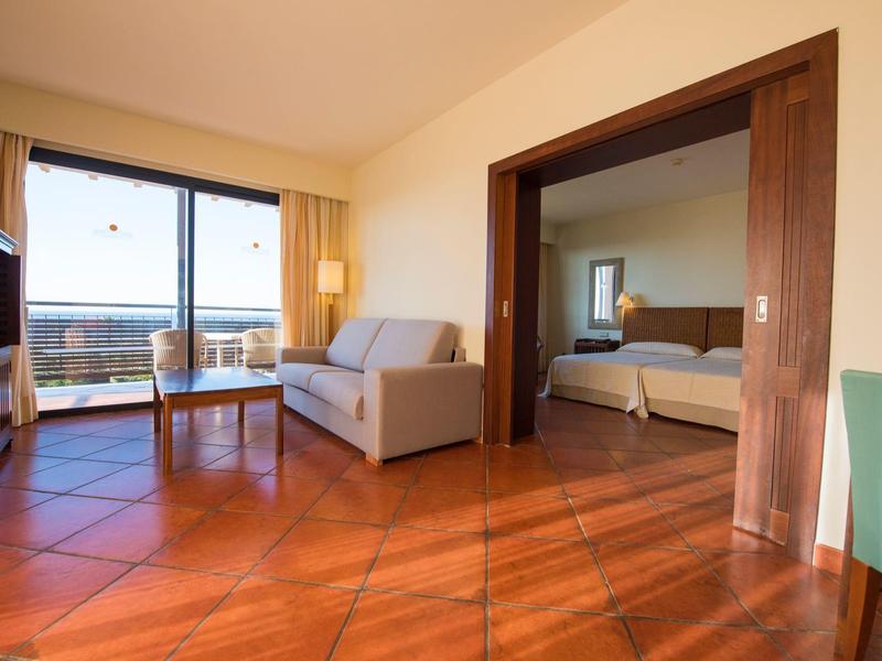 Moderner Wohnraum mit Holzfliesen, Sofa, Glastisch, Terrasse und Blick auf angrenzendes Schlafzimmer.