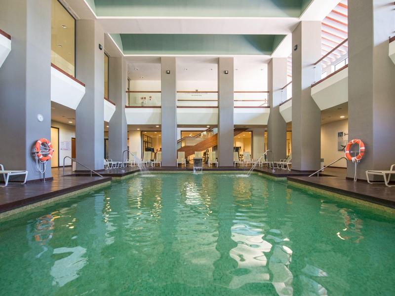 Moderner Innenpool mit grünlichem Wasser, hohen Säulen und Liegestühlen an den Seiten.