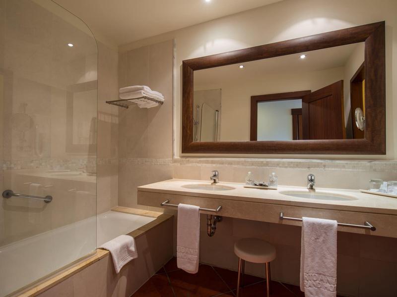 Helles Badezimmer mit Badewanne, Doppelwaschbecken, großem Spiegel und zwei Handtüchern.