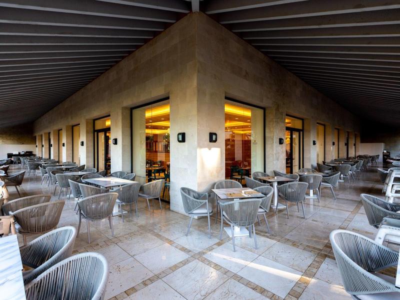 Große Terrasse mit vielen grauen Stühlen und Tischen, modernem Dach und warm beleuchteten Innenräumen.