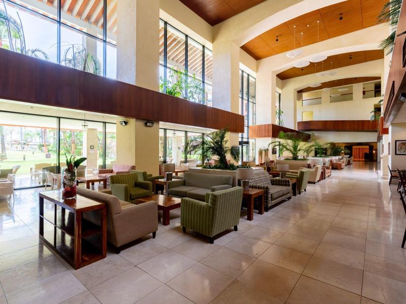 Großer, heller Lobbybereich mit Polstermöbeln, hohen Fenstern und holzverkleister Decke.