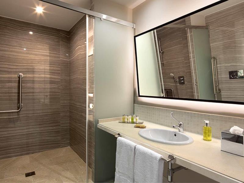 Modernes Badezimmer mit großer Glas-Dusche, Waschtisch, Spiegel und graubraunen Fliesen.