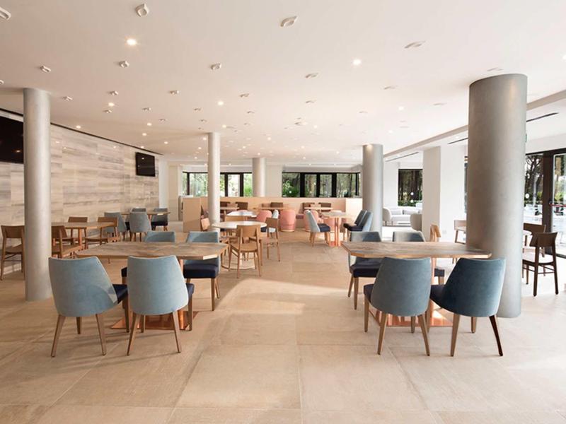 Moderner, heller Gastraum mit blauen Stühlen, Holztischen und großen Fenstern.