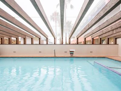 Piscina coperta con acqua azzurra limpida, travi in legno sul soffitto e finestre laterali per la luce naturale.