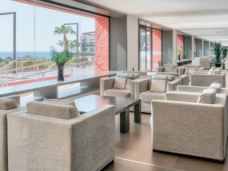 Moderner heller Sitzbereich mit beigen Sesseln, großem Fenster und Blick auf Terrasse und Meer.