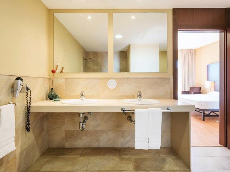 Helles Badezimmer mit Doppelwaschbecken, großen Spiegeln und beige-braunen Fliesen.