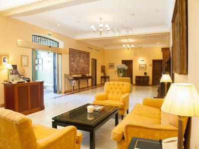 Przytulny hol hotelowy z żółtymi fotelami, drewnianymi stolikami i ciepłym oświetleniem.