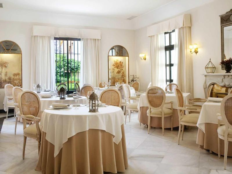 Elegantes Restaurant mit runden Tischen, beige Tischdecken, bequemen Stühlen und großen Fenstern.