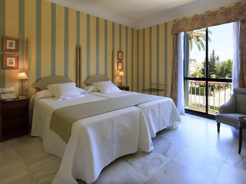 Helles Schlafzimmer mit zwei Einzelbetten, gestreifter Wandgestaltung und großem Fenster mit Balkon.