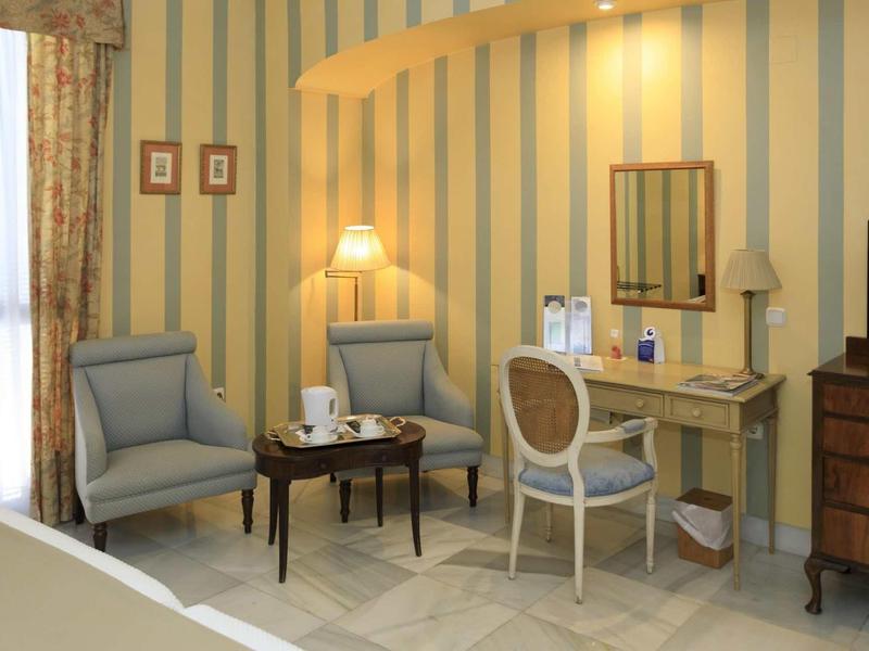 Gemütliche Zimmerecke mit zwei blauen Sesseln, Holztisch, Schminktisch und gestreifter Tapete.