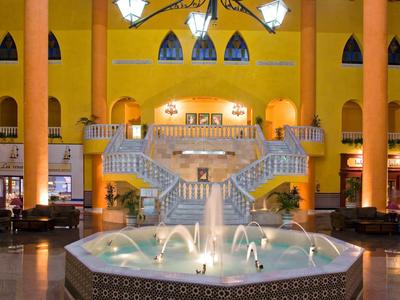 Ampia hall d'albergo con pareti gialle, fontana centrale e grande scala curva