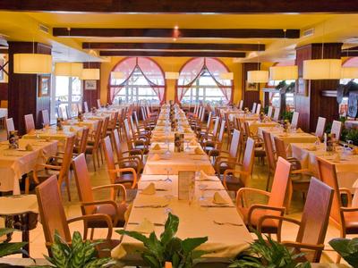 Ampia sala ristorante con lunghi tavoli apparecchiati e mobili in legno con illuminazione calda.