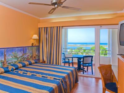 Stanza d'hotel con due letti, vista mare e balcone con tavolo e sedie.