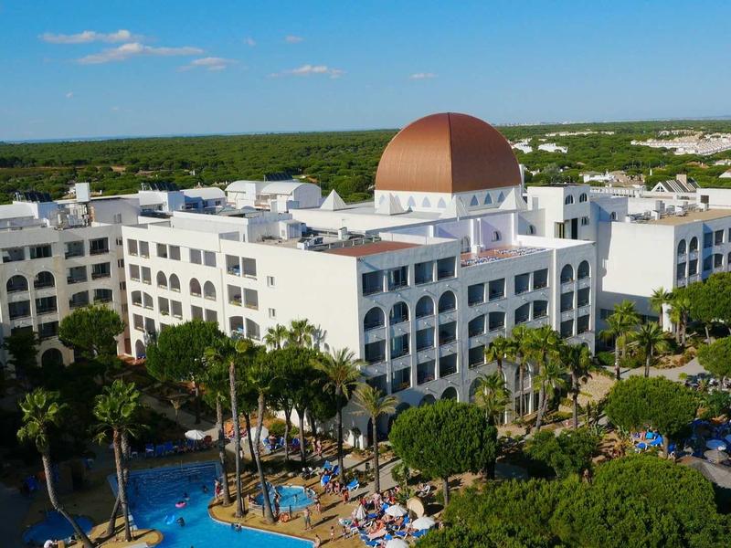 Großes weißes Hotel mit kupferner Kuppel, umgeben von Bäumen und einem Pool