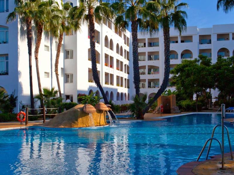 Hotel mit großem Pool und Palmen bei klarem Himmel.