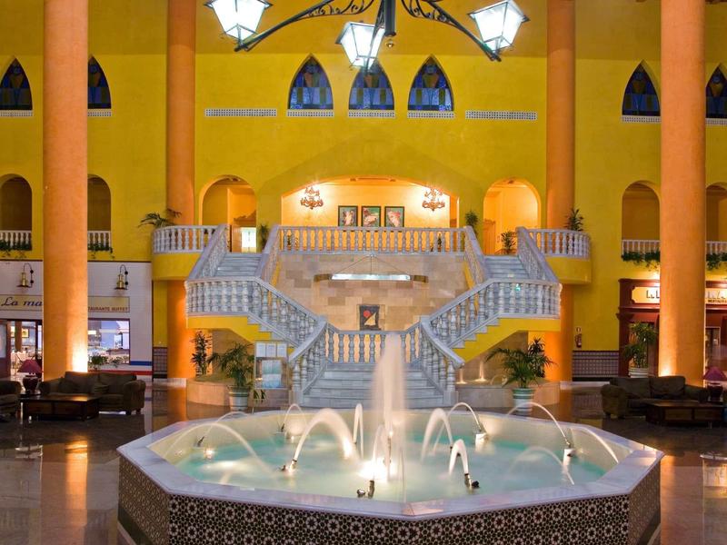Großer Hotel-Lobbybereich mit Springbrunnen und symmetrischer Treppe in warmem Licht.