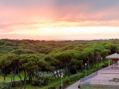 Sonnenuntergang über einem grünen Wald mit klaren Wegen neben einem Gebäude mit Terrassen.
