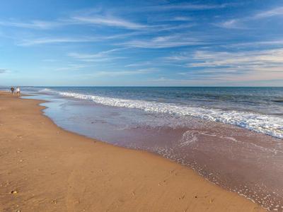 Breiter Sandstrand mit sanften Wellen und blauem Himmel mit vereinzelten Wolken.