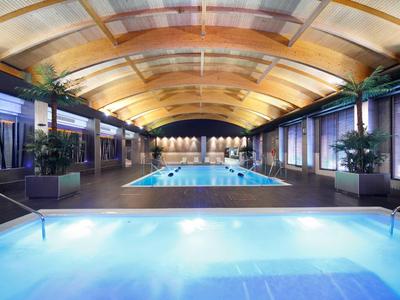 Helles Schwimmbad mit Holzdecke, beleuchtet, Pflanzen und bequemen Sitzplätzen innen.