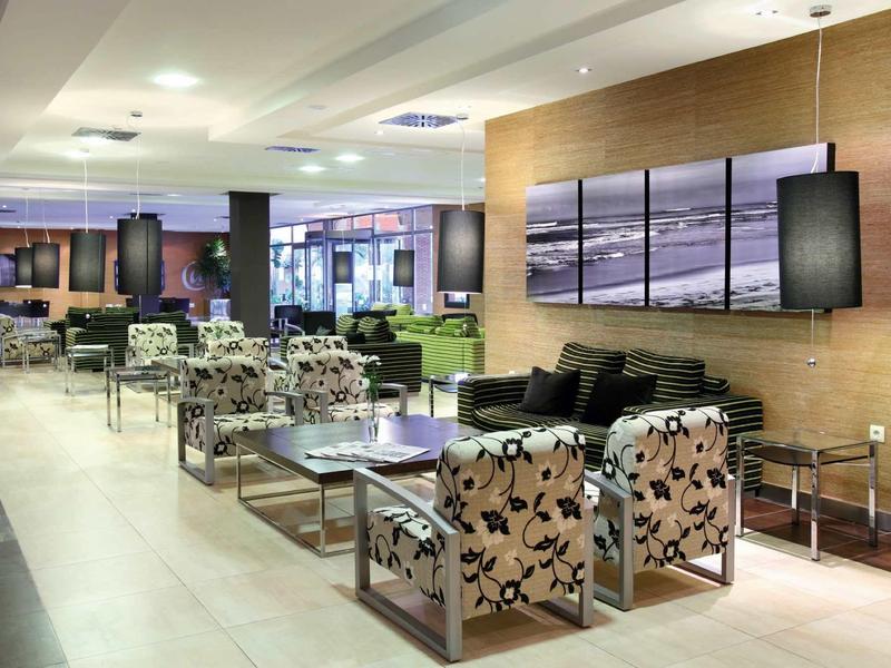 Moderner Lounge-Bereich mit gemusterten Sesseln, Holzwand und großen Fenstern bei Tageslicht.