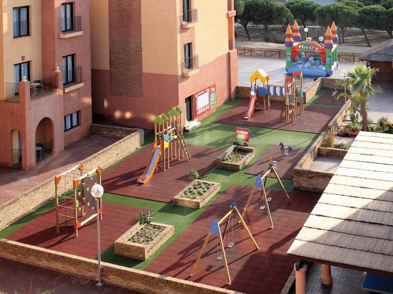 Ein bunter Spielplatz mit Rutschen, Schaukeln und Klettergerüsten neben einem Wohnhaus.