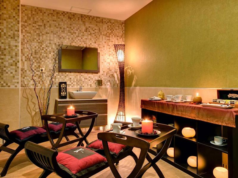 Gemütlicher Raum mit warmem Licht, grünen Wänden, Holzmöbeln und zwei Sesseln mit roten Kissen.