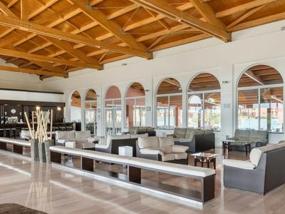 Světlý hotelový salon s moderním posezením, dřevěným stropem a barem v pozadí.