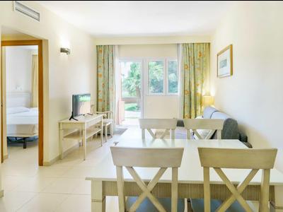 Světý obývací pokoj s jídelním stolem, pohovkou, televizí a výhledem na zahradu oknem.