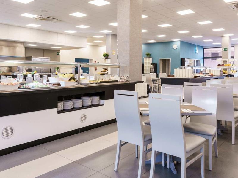 Moderne Kantine mit weißen Stühlen, langen Tischen und hellem Beleuchtungssystem.