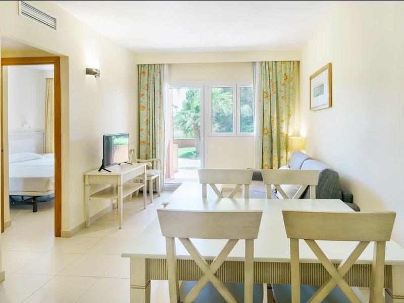 Helles Wohnzimmer mit Essbereich, Sofa, TV, großem Fenster und Blick ins Grüne.