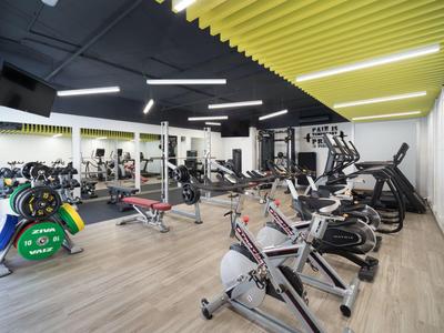 Salle de sport moderne avec haltères, vélos d'appartement et machines cardio dans une pièce lumineuse.