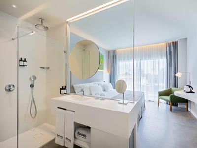 Helles Hotelzimmer mit modernem Bad, Dusche, großem Spiegel, Bett und Balkon mit Blick.