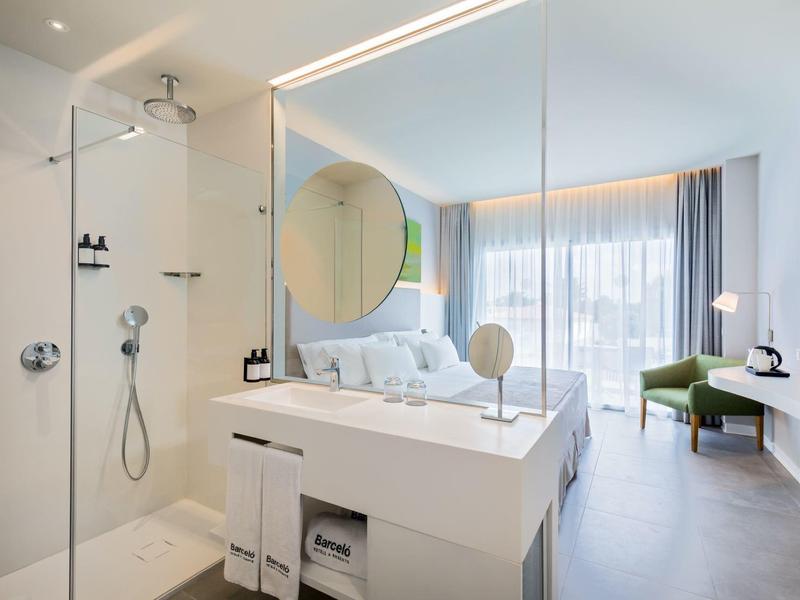 Helles Hotelzimmer mit modernem Bad, Dusche, großem Spiegel, Bett und Balkon mit Blick.