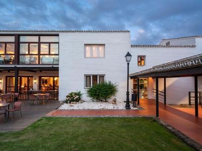 Nowoczesny zewnętrzny obszar hotelu z tarasem, trawnikiem i nastrojowym oświetleniem o zmierzchu.