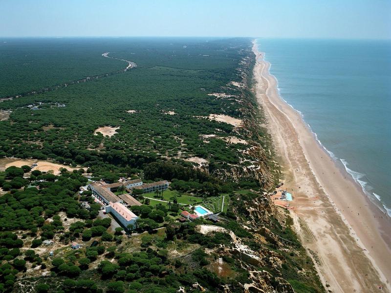 Langer Strand und angrenzende grüne Landschaft mit wenigen Gebäuden am Meer.