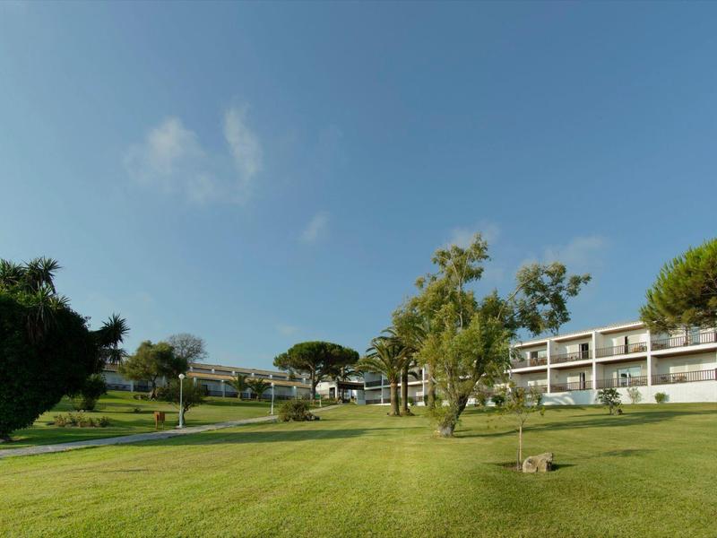 Großes grünes Rasenfeld mit Bäumen und modernem Hotelgebäude im Hintergrund bei klarem Himmel.