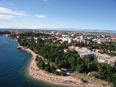 Küstenstadt mit Sandstrand, grünen Bäumen und dicht bebautem Stadtgebiet unter blauem Himmel.