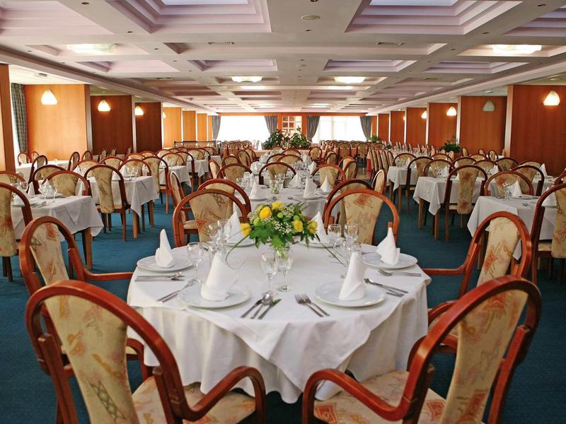 Tavoli rotondi elegantemente apparecchiati in una grande sala da banchetti con pannelli in legno.