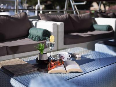 Accogliente terrazza con divano, tavolo, libro aperto, tazza da caffè e piante decorative.