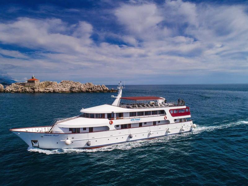 Nave da crociera bianca sul mare blu con costa rocciosa sullo sfondo.