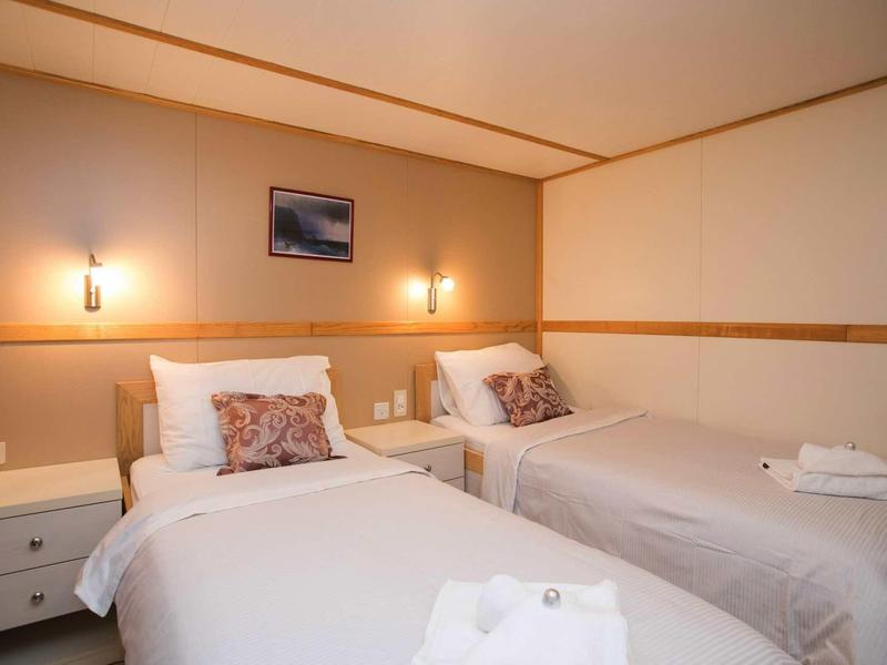 Camera doppia con due letti singoli, comodino e cuscini morbidi con illuminazione calda.