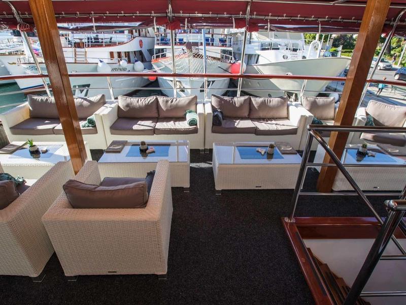 Area esterna di un bar dell'hotel con sedute bianche e vista su una marina con barche.