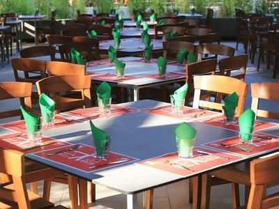 Restaurant mit Holztischen und -stühlen, Tischen mit grünen Servietten und Menükarten gedeckt