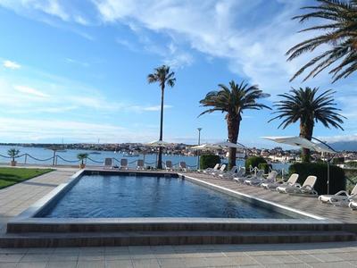 Ein rechteckiger Pool mit Palmen und Liegestühlen unter blauem Himmel am Meer.