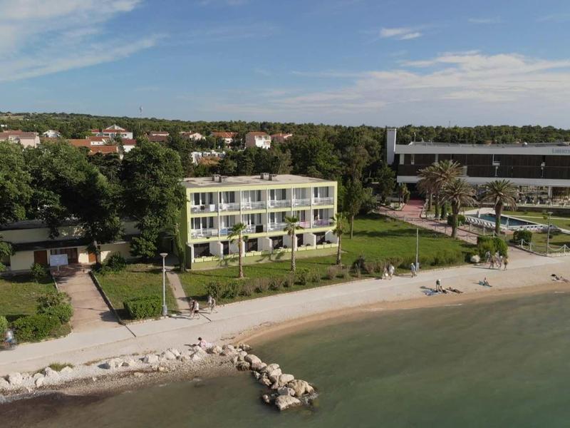 Edificio dell'hotel con balconi sulla spiaggia e piscina adiacente sotto un cielo sereno.
