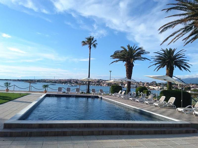 Piscina con lettini, palme e vista mare sotto un cielo limpido.