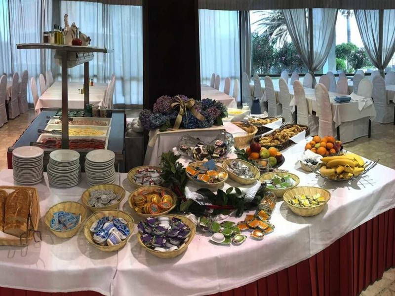 Buffet con vari cibi in una sala per eventi con tavoli apparecchiati.